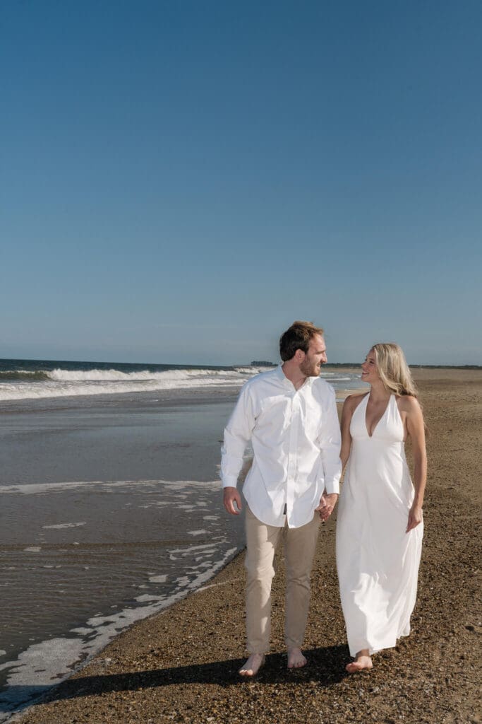 Couple walking barefoot along the shoreline during a romantic beach engagement session in Delaware
